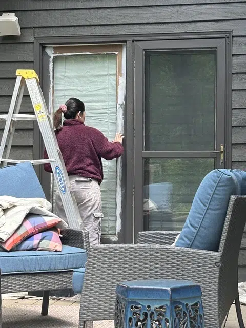 Painter masking patio door frame on dark siding wall — Father And Son Custom Painting in Raleigh